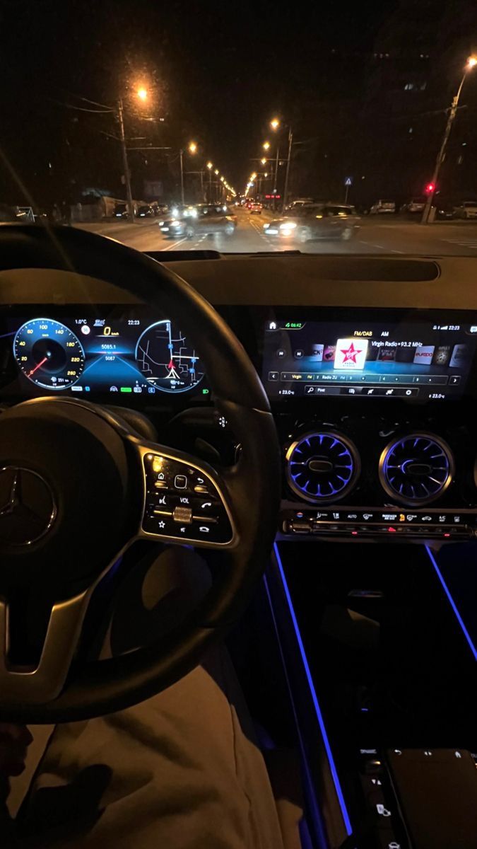 the interior of a car with dashboard lights and steering wheel controls on at night time