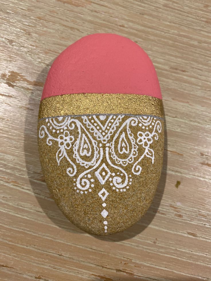 a pink and gold painted rock sitting on top of a wooden table