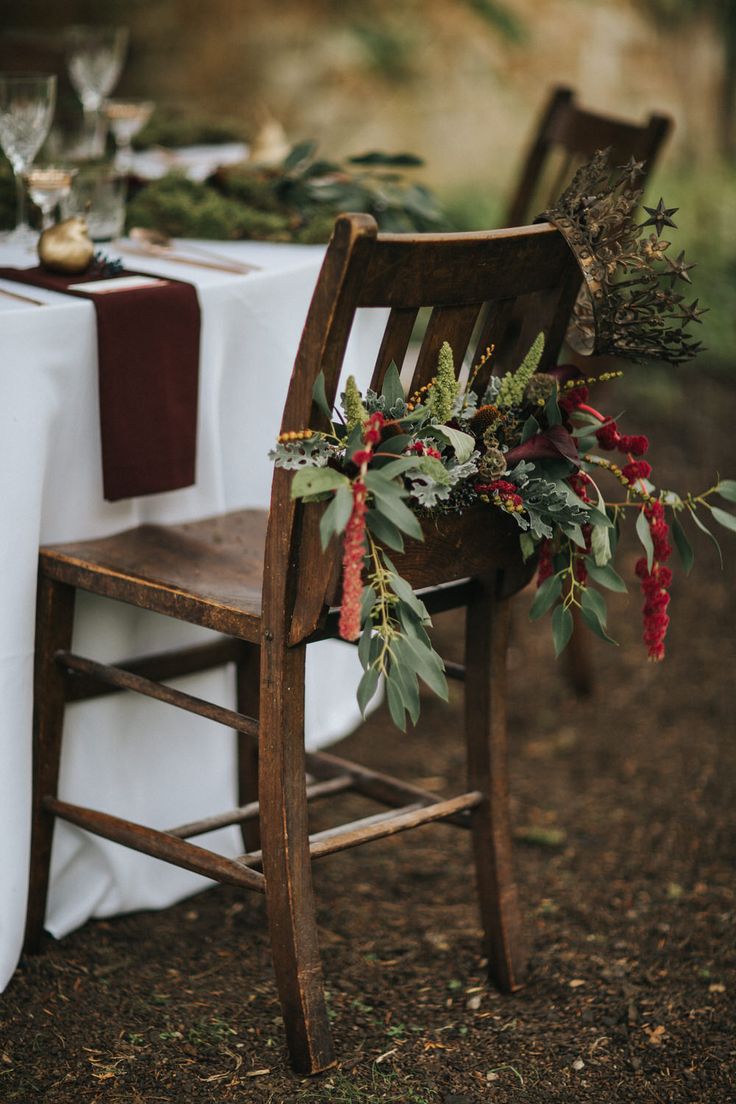 a wooden chair sitting next to a table covered in white cloths and greenery