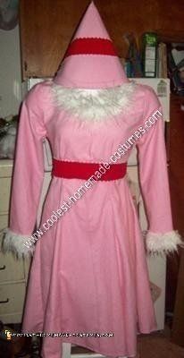 a pink dress with white fur on the collar and red trimmings is displayed in front of a wooden cabinet