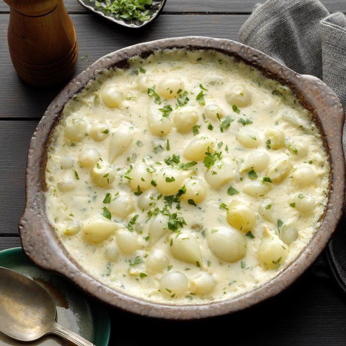 a bowl filled with macaroni and cheese on top of a wooden table next to two silver spoons