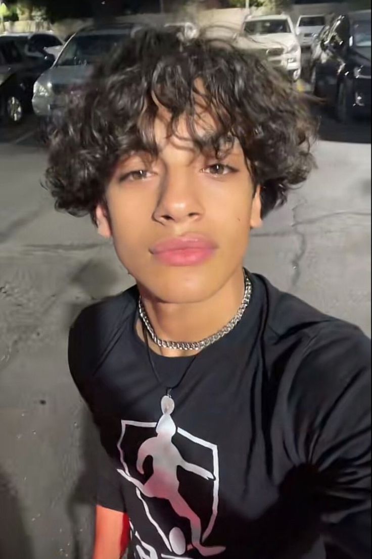 a man with curly hair wearing a black t - shirt and looking at the camera