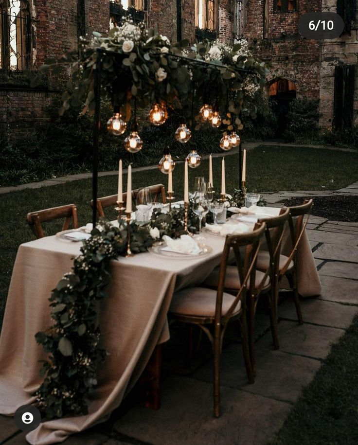 a long table with candles and flowers on it in front of an old brick building