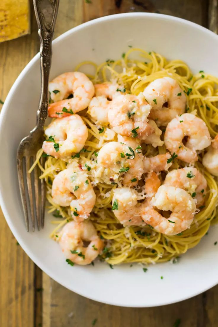 pasta with shrimp and parsley in a white bowl on top of a wooden table