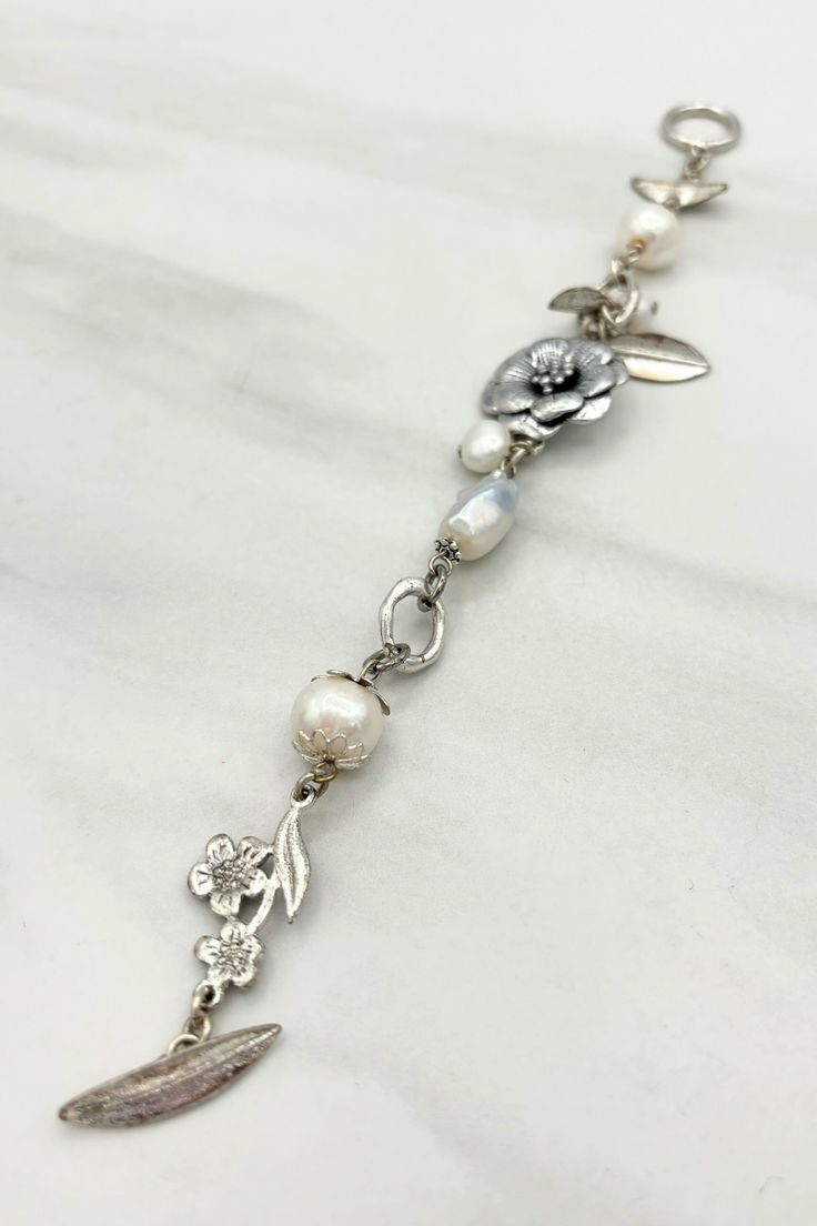 This charming bracelet features dainty flowers and pearls, making it the perfect accessory for any occasion. With its subtle shimmer and delicate design, this bracelet is sure to add a touch of whimsy to any outfit. (Cutesy and playful, this bracelet is a must-have for any jewelry collection!) Details:- Genuine Freshwater Pearl Beads- Nature and Flora Inspired Elements- Non-Adjustable Dimensions:- Total Length: 8" Adjustable Flower-shaped Pearl Jewelry, Feminine Pearl Drop Bracelets, Elegant White Bracelets With Flower Charm, Delicate Beaded Bracelets With Pearl Charm, Delicate Pearl Charm Bracelet Jewelry, Delicate White Flower Pearl Bracelet, White Dainty Metal Pearl Bracelet, White Dainty Pearl Bracelet, Silver Dainty Pearl Bracelet