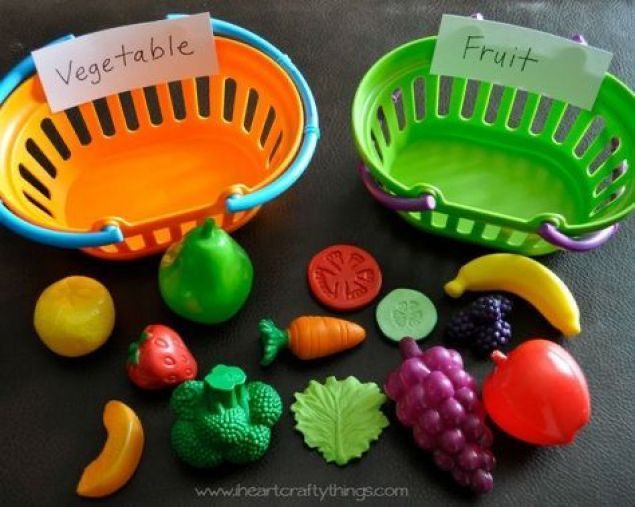 two plastic fruits and vegetables in baskets on a table with labels that read vegetable fruit