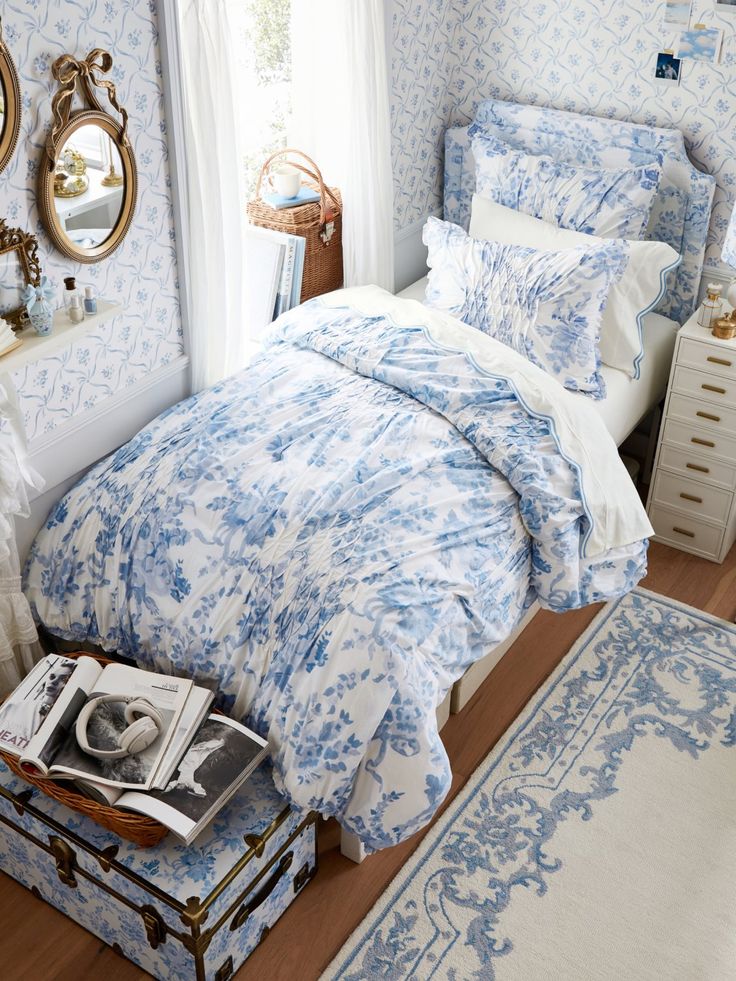 a bedroom with blue and white bedding, mirror, dresser and chest of drawers