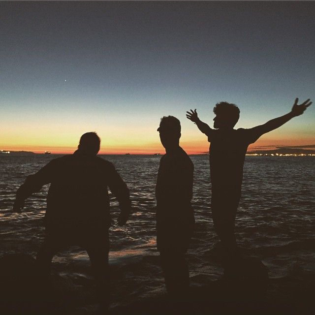 three men standing on the beach at sunset with their arms in the air and one man raising his hands up