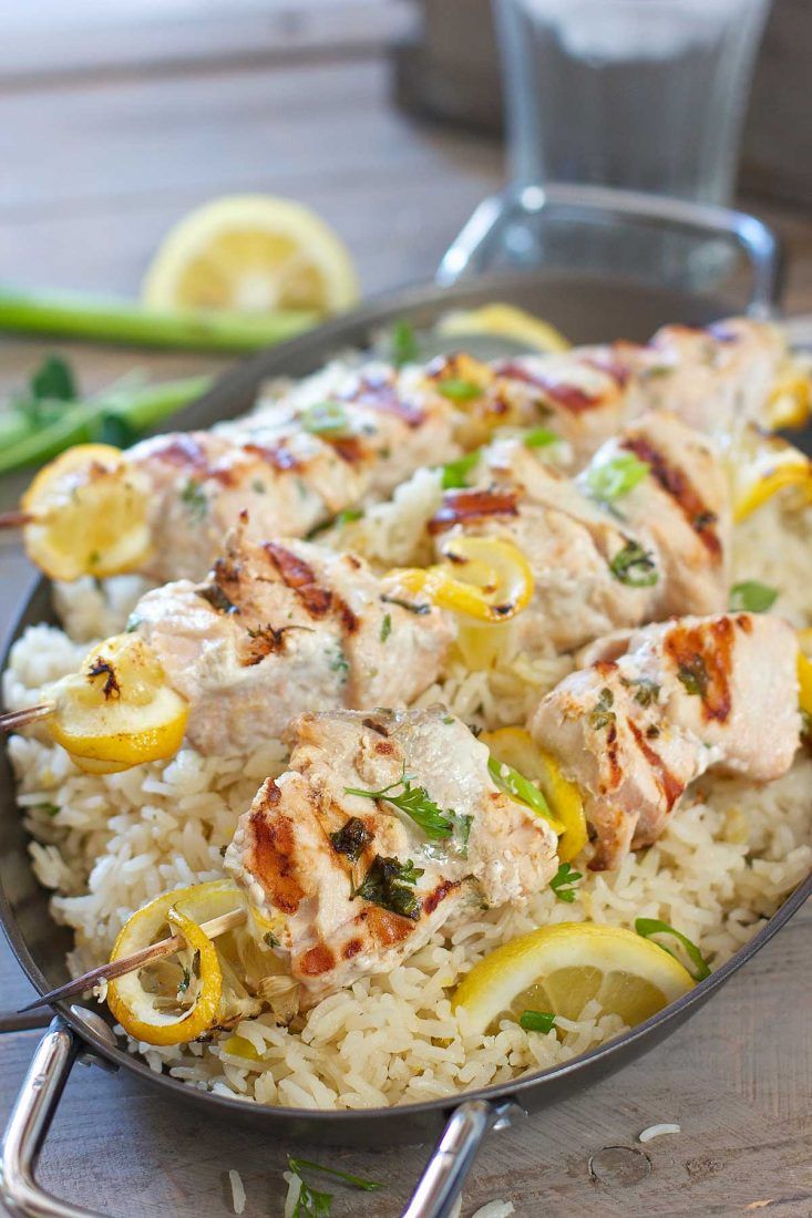 greek salmon kabobs with oven baked lemon rice in a skillet on a wooden table