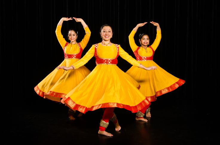 three girls in yellow and red dresses are performing on stage with their hands up to the side