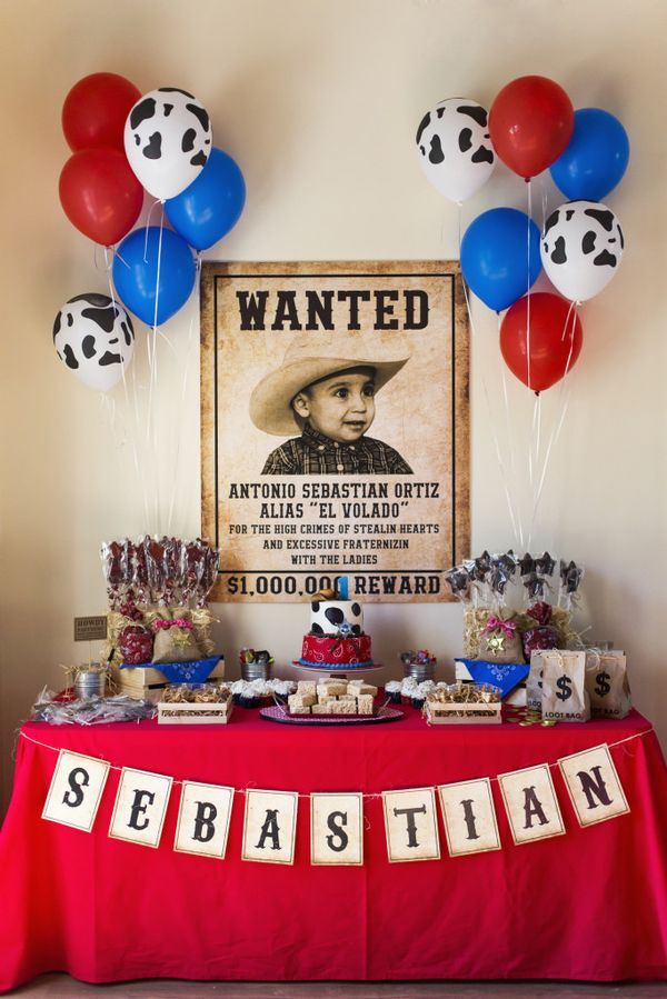 a red table topped with lots of balloons next to a sign and cow print on the wall