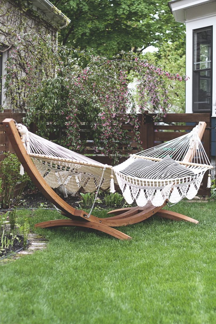 a hammock sitting on top of a wooden stand in the grass next to a house