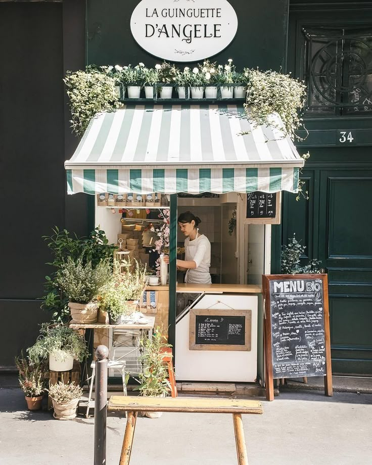 the outside of a small shop with flowers and plants in it's front window