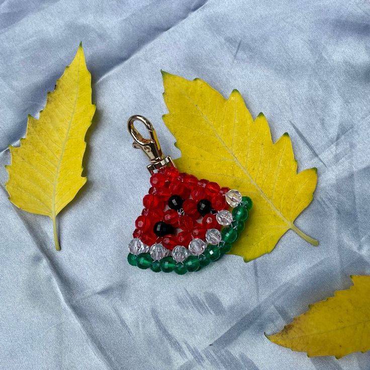 a red, green and white beaded keychain sitting on top of a leaf