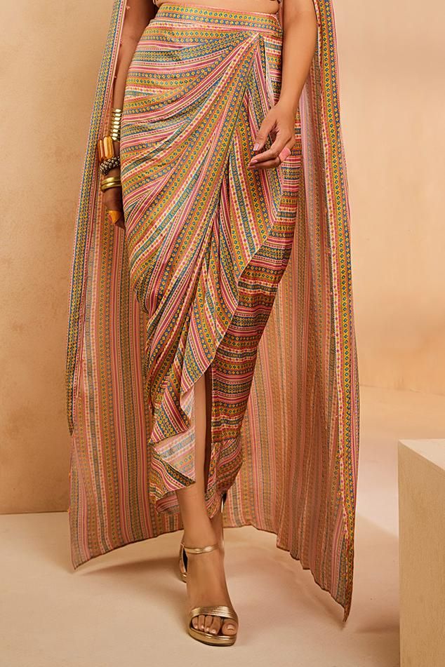 Multi colored boho-stripe printed cape blouse with sequins and threadwork embroidery. Comes with matching printed overlap ruffle skirt. 
Components: 2
Pattern: Printed, Hand Embroidered
Type Of Work: Striped, Sequins, Thread Work
Neckline: V Neck
Sleeve Type: Cape Sleeves
Fabric: Crepe
Color: Multi Color
Other Details: 
Note: All the jewellery worn by the model is not for sale
Occasion: Destination Wedding - Aza Fashions Boho Cape, Threadwork Embroidery, Cape Blouse, Cape Sleeves, Thread Work, Colorful Boho, Ruffle Skirt, Set For Women, Aza Fashion