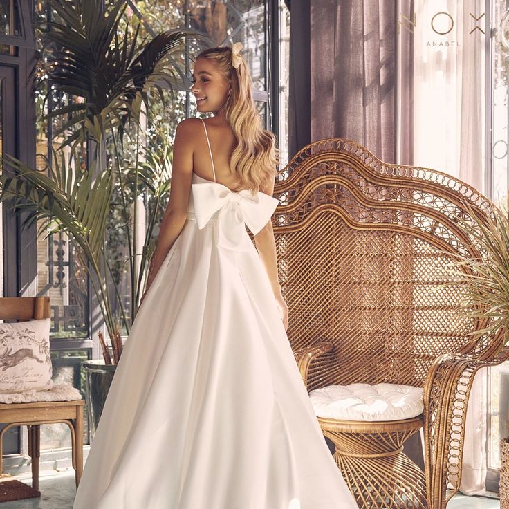 a woman in a white wedding dress standing next to a wicker chair and palm tree