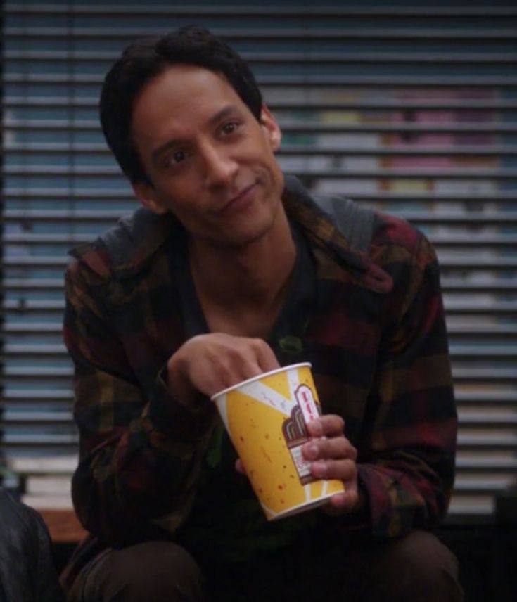 the young man is holding a drink in his hand and smiling at the camera while sitting down