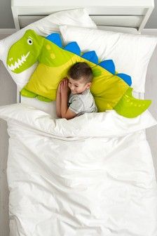 a young boy laying in bed under a green and blue pillow with an alligator on it