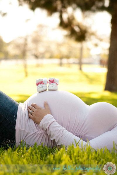 a pregnant woman laying in the grass with her shoes on her belly