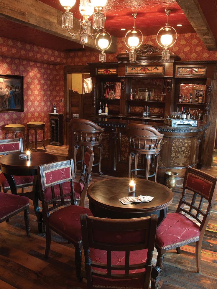 a dimly lit restaurant with red chairs and wooden tables, chandeliers above the bar