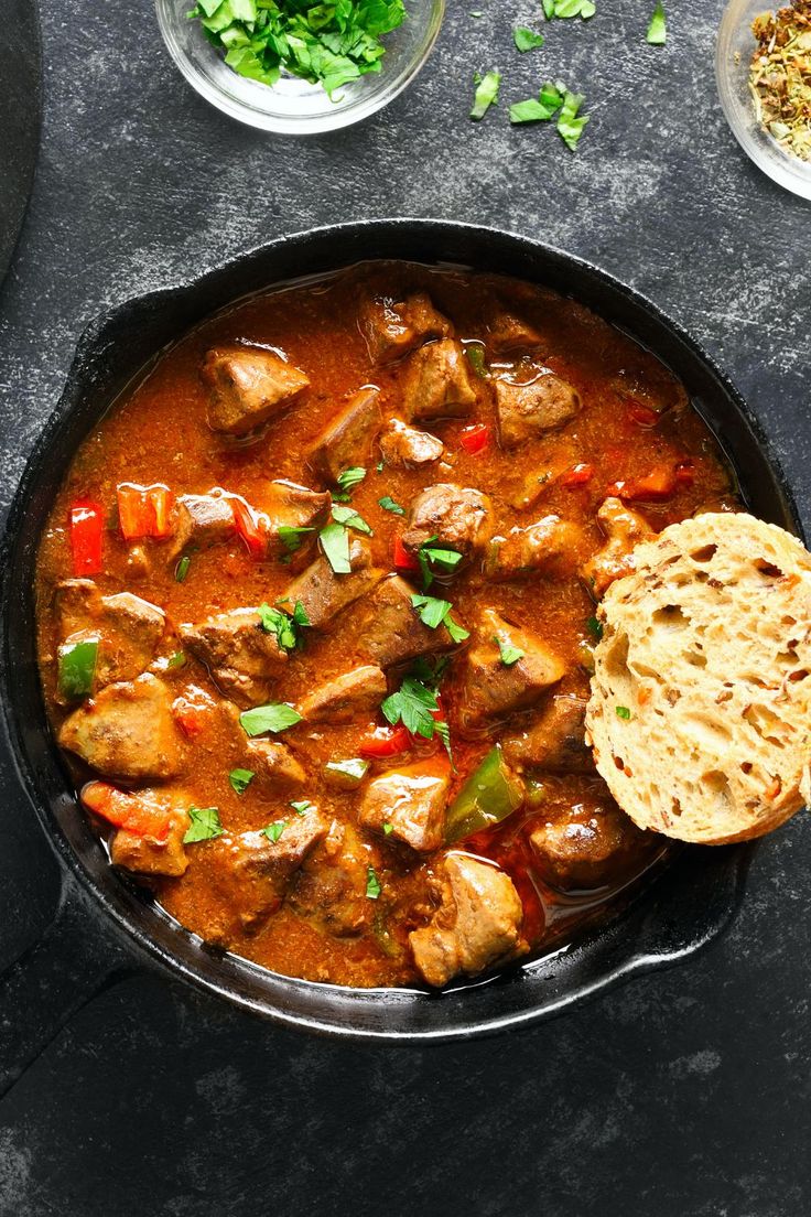 a skillet filled with meat and vegetables next to bread on a table, ready to be eaten