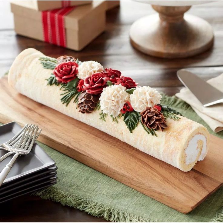 a roll decorated with flowers and pine cones on a cutting board next to silverware