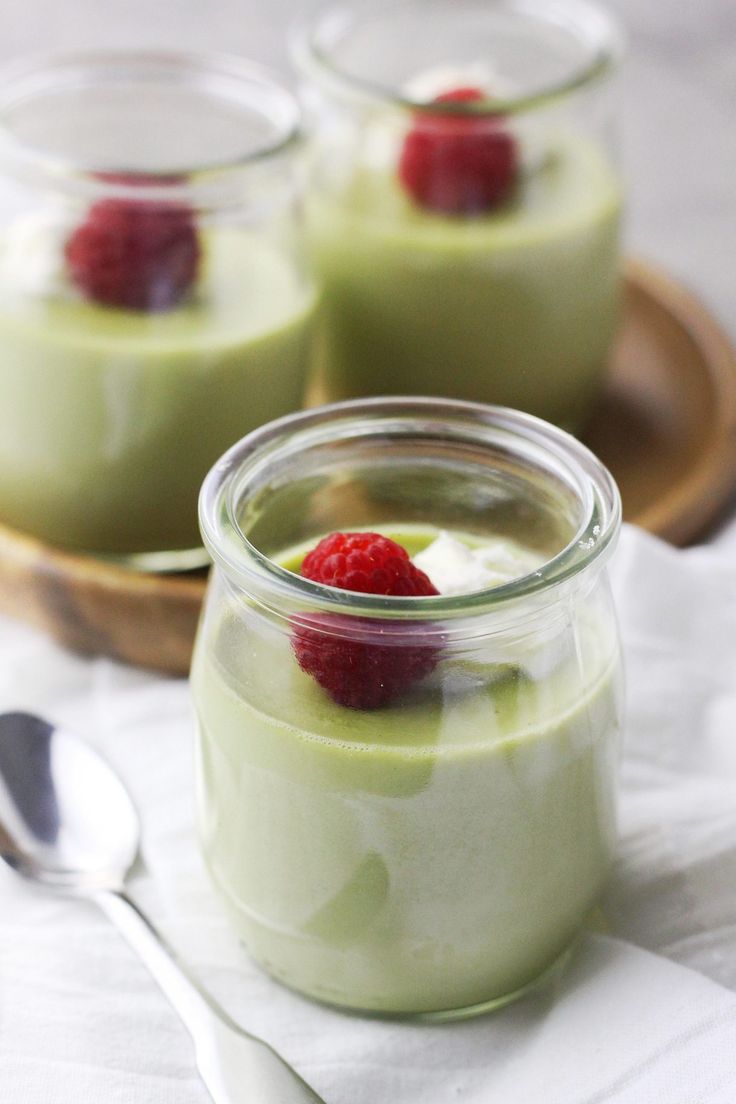 three desserts with raspberries and custard in small jars on a table