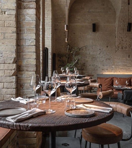 an empty restaurant with wooden tables and leather chairs, brick walls and exposed ceilinging