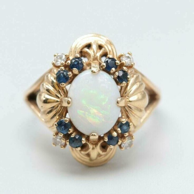 an opal and diamond ring with blue sapphires on the sides, set in yellow gold