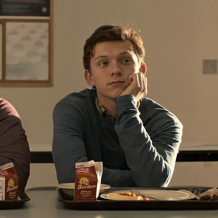 two young men sitting at a table with food in front of them and one is holding his hand to his chin