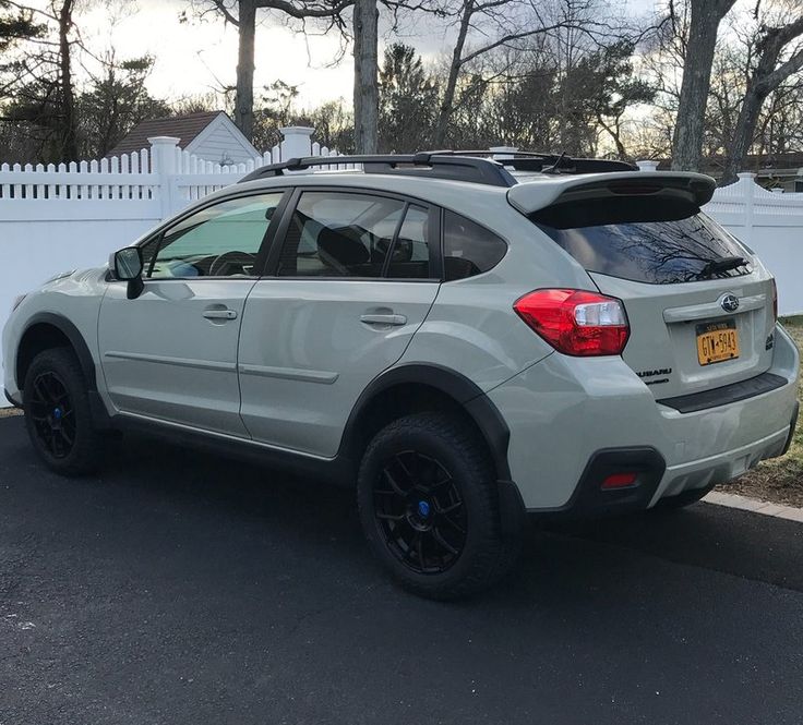 a white subarunt parked on the street in front of a white picket fence