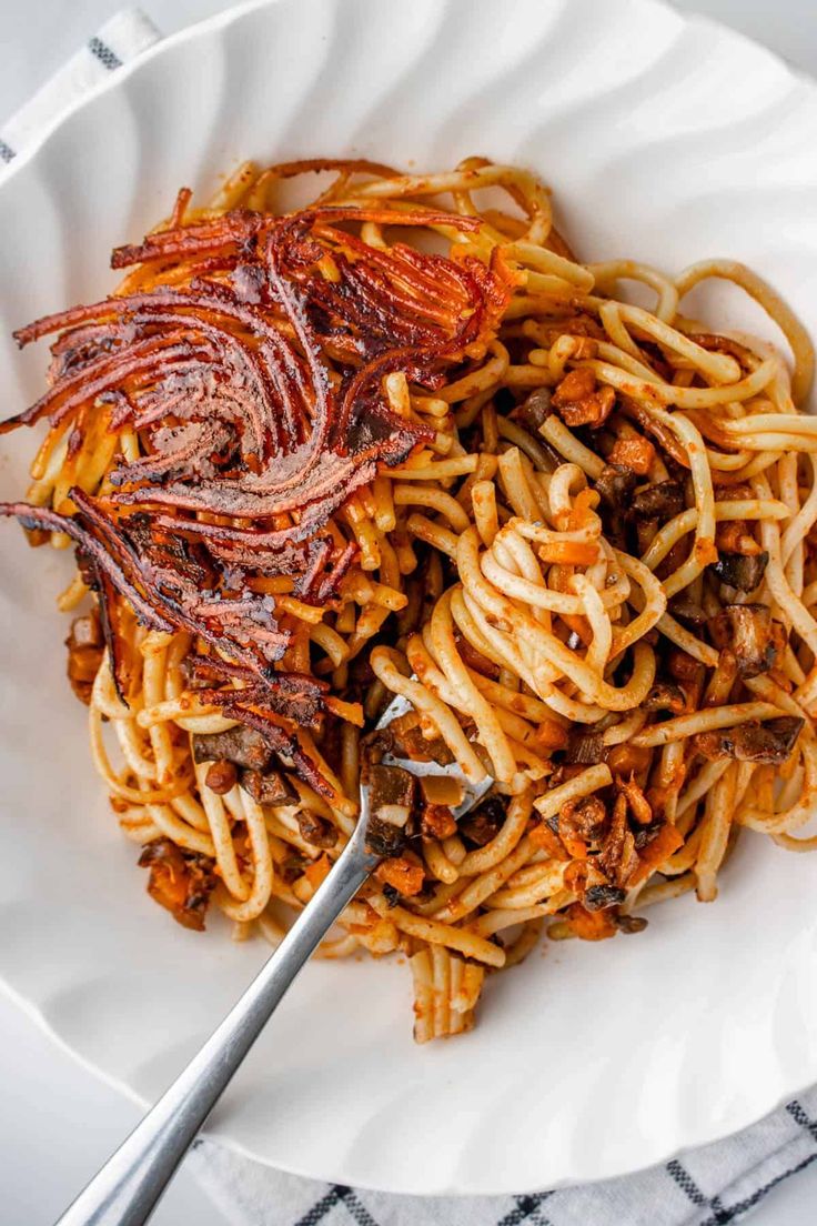 a white plate topped with spaghetti and meat next to a fork on top of a table