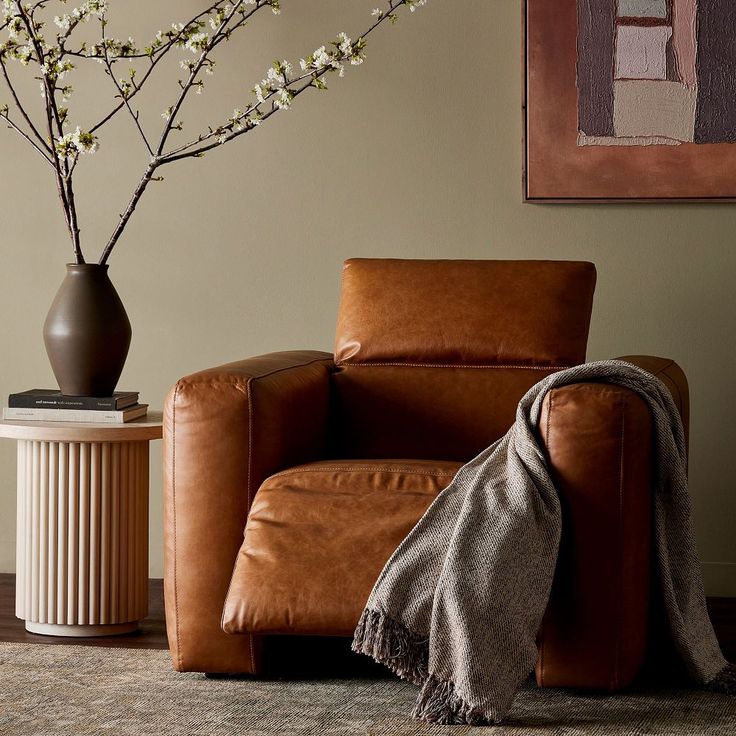 a brown leather chair sitting next to a vase with white flowers on top of it