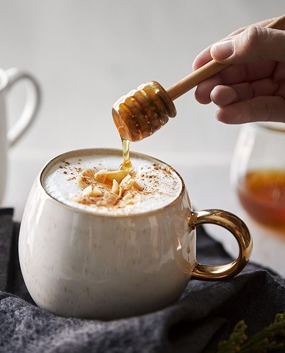 a person pouring honey into a mug with cinnamon on the rim and spoon in it