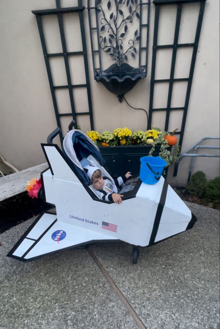 a small child in a toy space shuttle with flowers and potted plants behind it