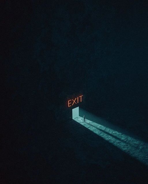 a person standing in the dark with an exit sign lit up behind them that says exit