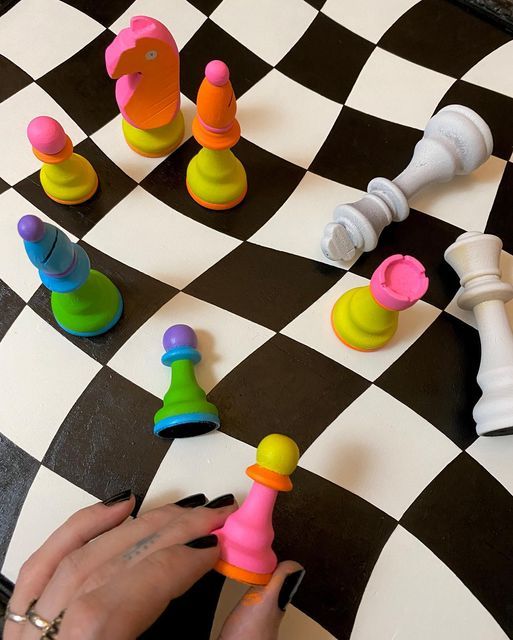 a person is playing chess on a black and white checkerboard board with colorful pieces