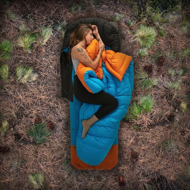 a woman laying on top of a blue and orange sleeping bag