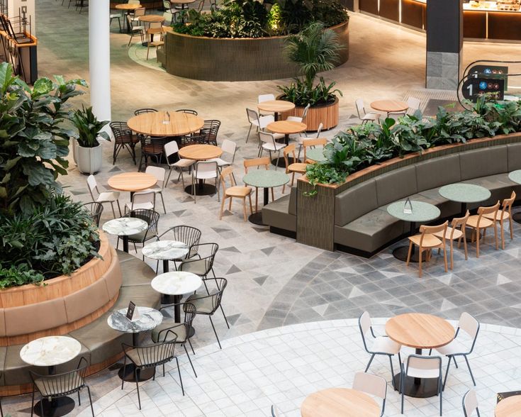 tables and chairs are arranged in the center of an indoor cafe with plants growing on the walls