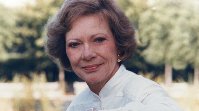 an older woman is smiling and posing for the camera with her arms crossed in front of her