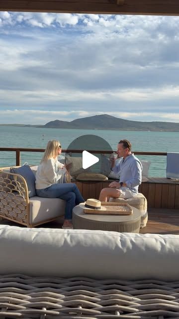 a man and woman sitting on top of a couch next to each other near the ocean