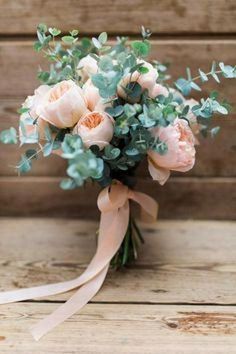 a bridal bouquet with peach roses and greenery on a wooden table in front of a wood wall