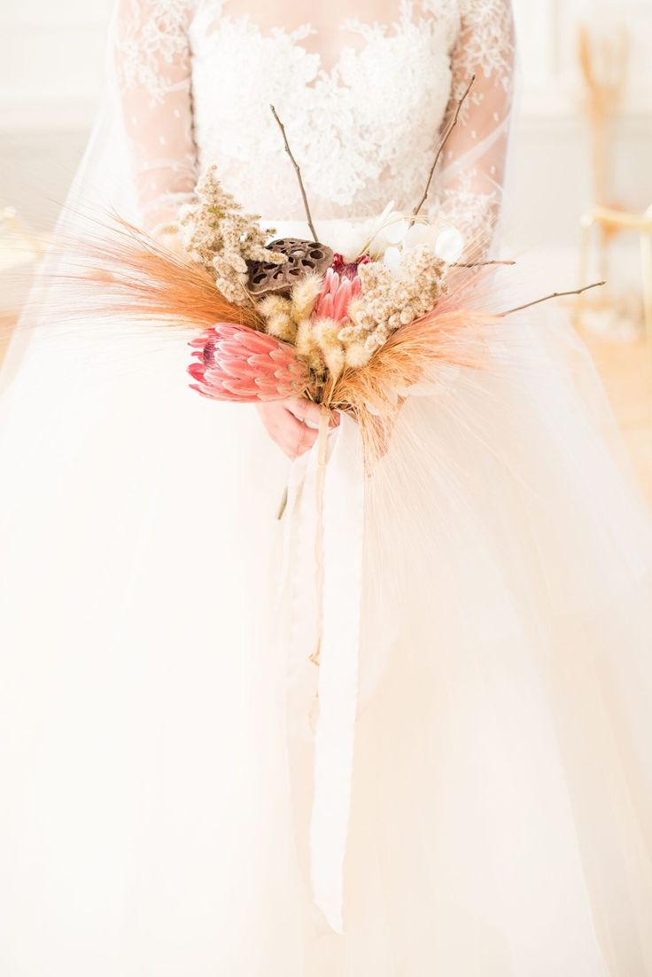 a woman in a white wedding dress holding a bouquet with feathers and flowers on it