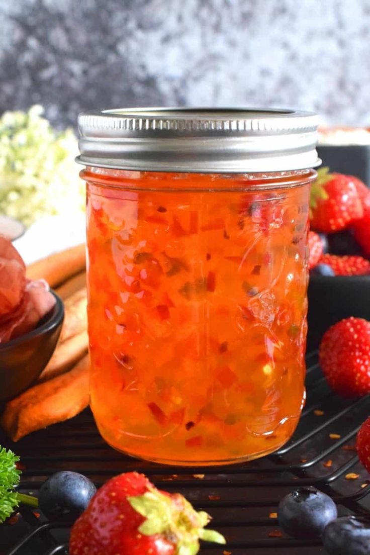 a jar filled with liquid sitting on top of a grill next to berries and carrots