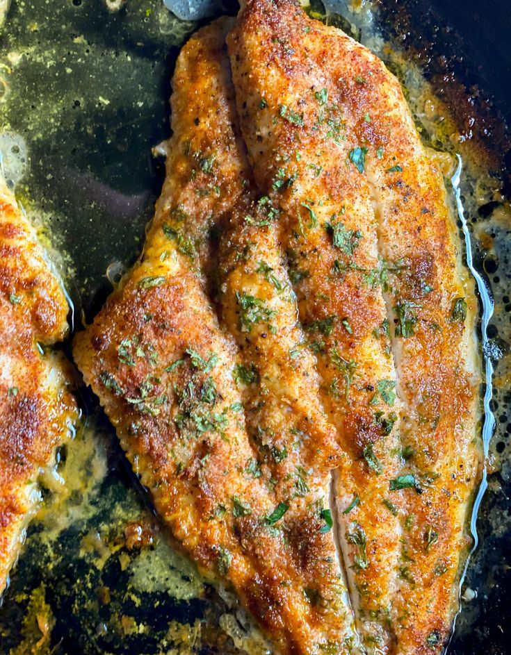 two pieces of meat are cooking in a frying pan on the stove top, with herbs sprinkled all over them