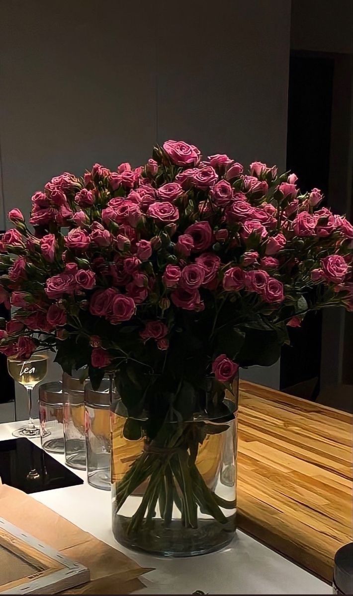 a vase filled with pink roses sitting on top of a wooden table next to two glasses