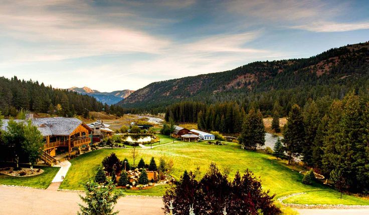 an aerial view of a home surrounded by trees and mountains in the distance is a large field with several houses on it