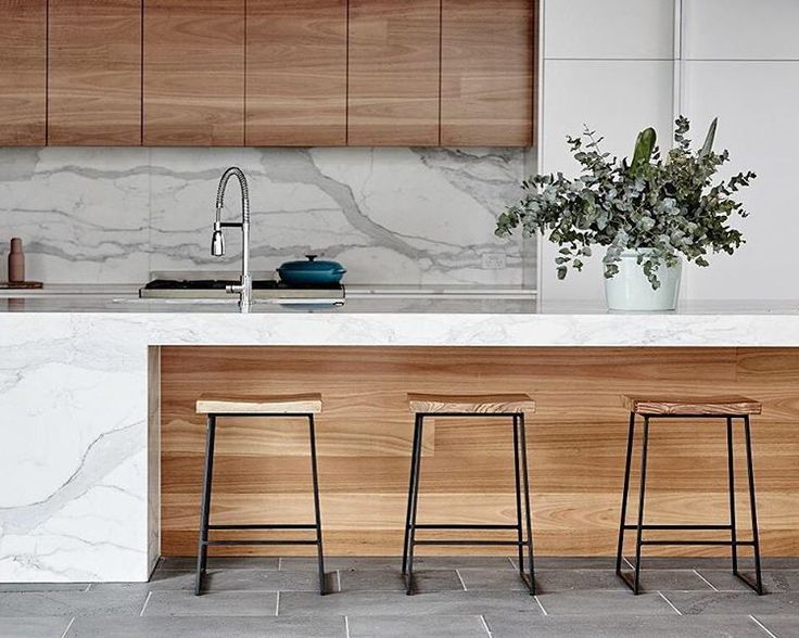 three bar stools sitting in front of a kitchen island with marble counter tops and wooden cabinets