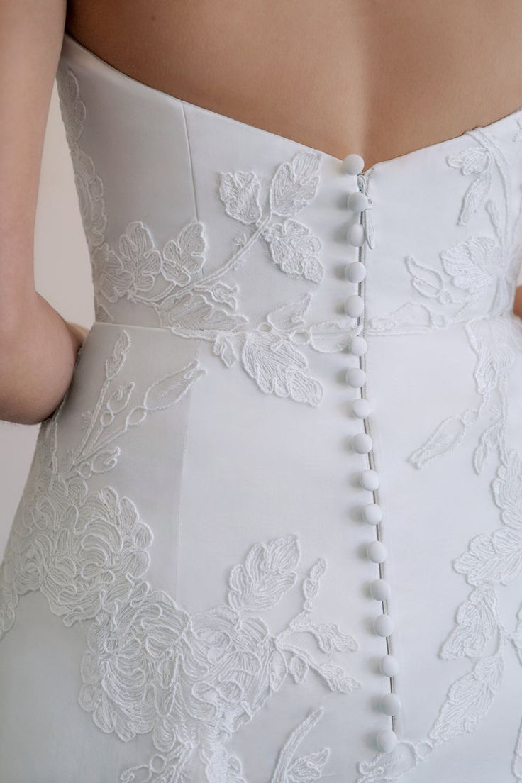 the back of a woman's wedding dress with white lace and buttons on it