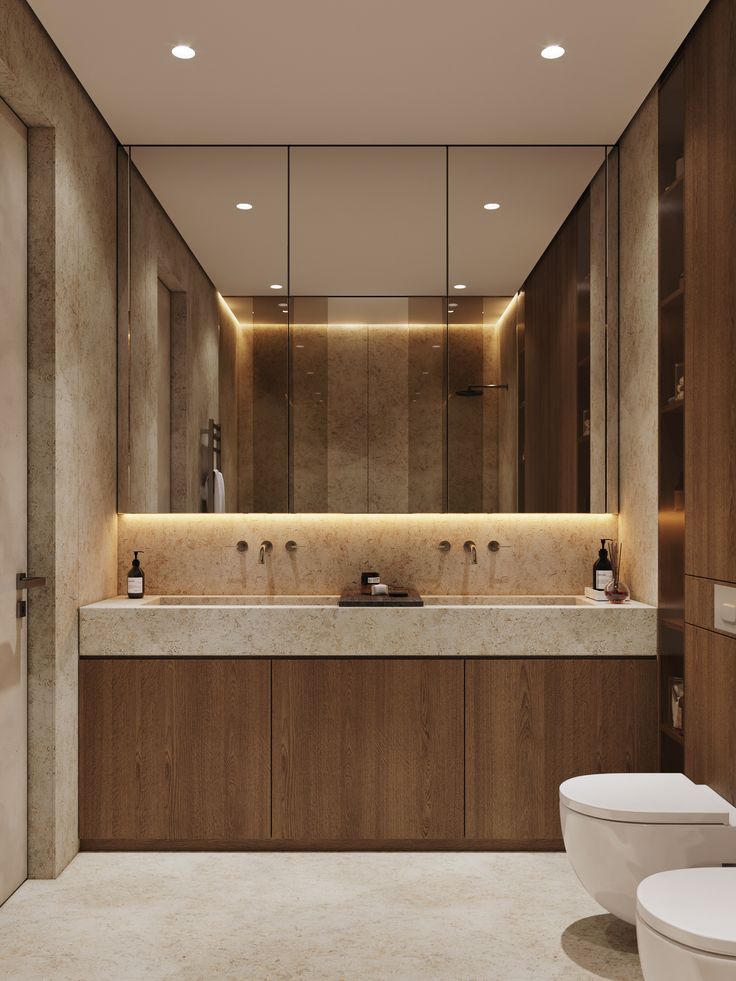 a bathroom with two toilets, a sink and a large mirror above the toilet is illuminated by recessed lights